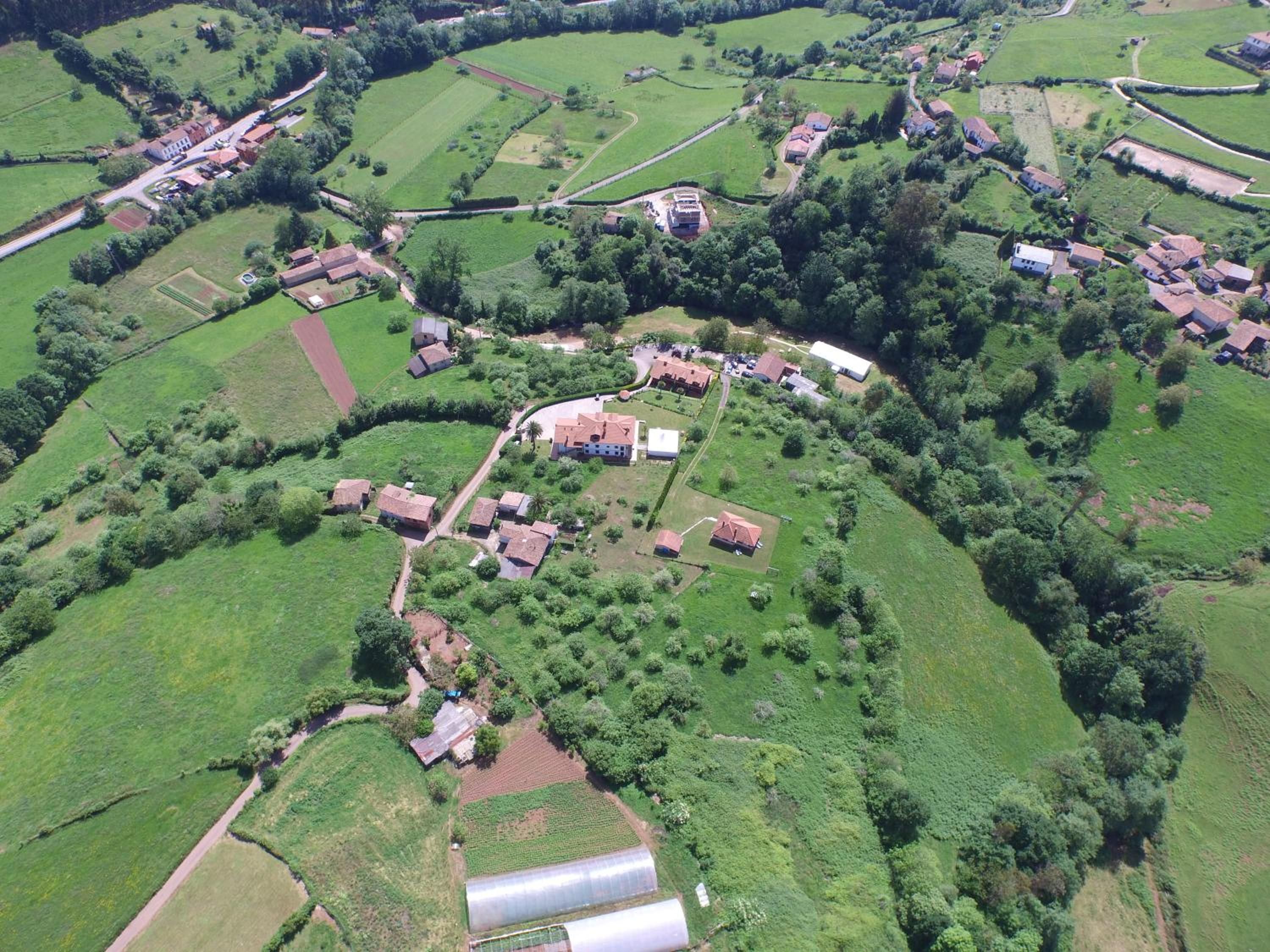 An aerial view of a rural area with scattered houses, fields, and a greenhouse.