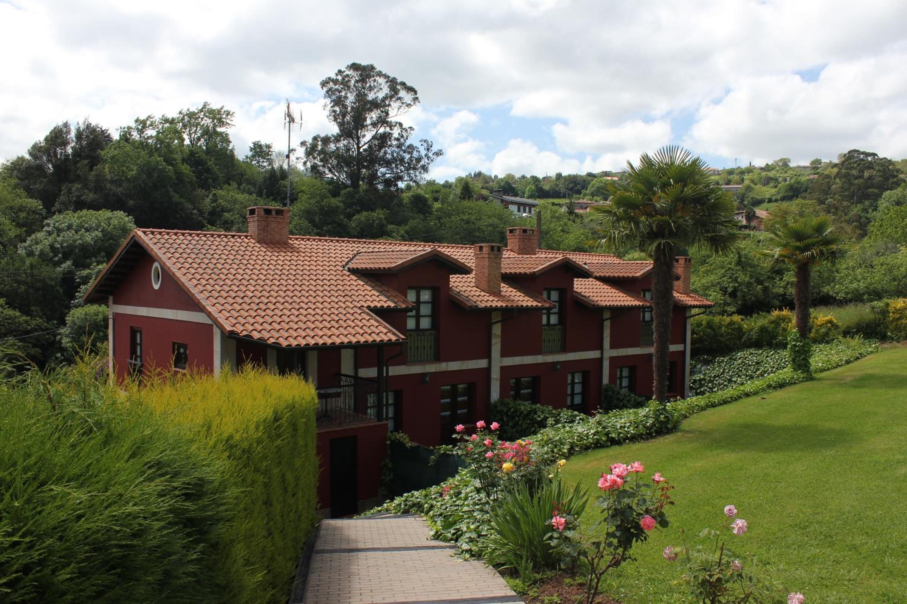 A red brick building with a tiled roof, surrounded by lush greenery and a well-maintained lawn.