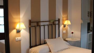 Un dormitorio ordenado con una cama, dos lámparas de noche, una mesita con un florero y un espejo en la pared.