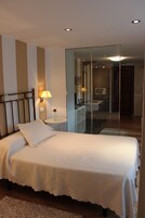A bedroom with a bed, bedside lamp, and a small table with a vase of flowers.