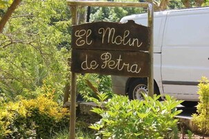 A wooden sign with the text "El Mlin de Petra" in a rustic font, surrounded by greenery and a white van in the background.