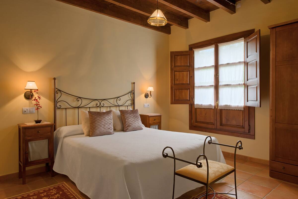 Quarto bem arrumado com cama, abajures, janela com persianas e guarda-roupa de madeira.