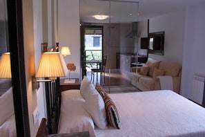 Habitación de hotel con cama, lámparas de noche, escritorio, silla, sofá y zona de cocina.