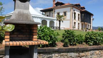A stone barbecue grill with a white tent and a two-story building in the background.