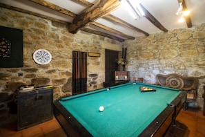 A billiards room with a pool table, dartboard, and a stone wall.