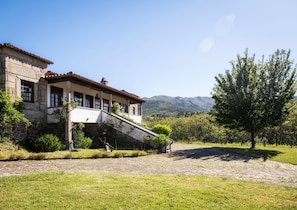 A stone building with a tiled roof, a stone staircase, and a grassy area with a tree.