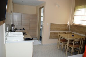 A compact kitchen with a sink, stove, and a small dining area with a table and chairs. - Triantafillas Apartments (Rhodes)
