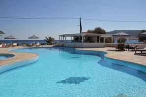 A swimming pool with lounge chairs and umbrellas, a covered seating area, and a view of the sea.