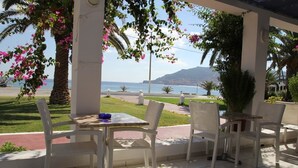 An outdoor patio with white wicker furniture, a view of the sea, and a mountain in the background. - Mediterranean Hotel (Karpathos)
