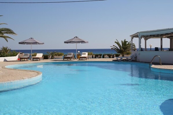 A swimming pool with lounge chairs and umbrellas, overlooking the sea.