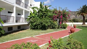 A white multi-story building with balconies, surrounded by lush greenery and flowering plants. - Mediterranean Hotel (Karpathos)