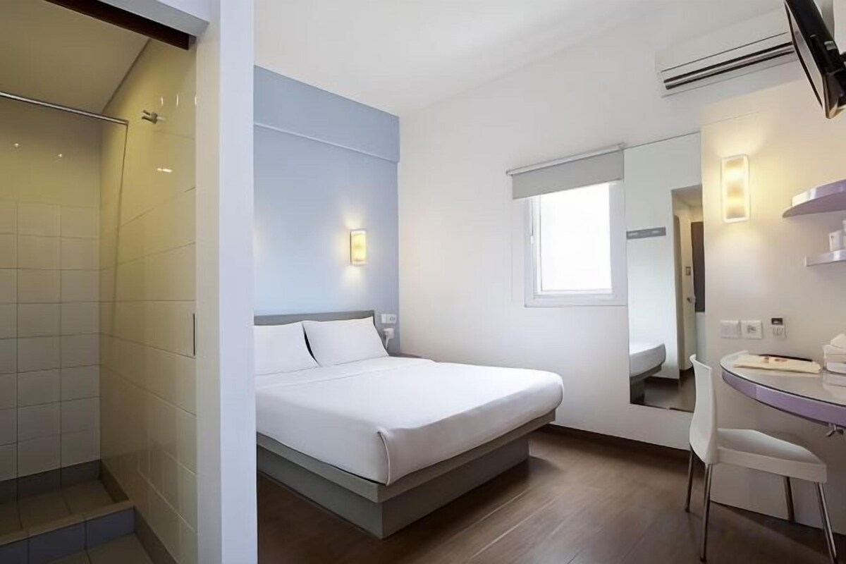 Et moderne hotelværelse med seng, brusebad, vaskebord med spejl og et vindue.