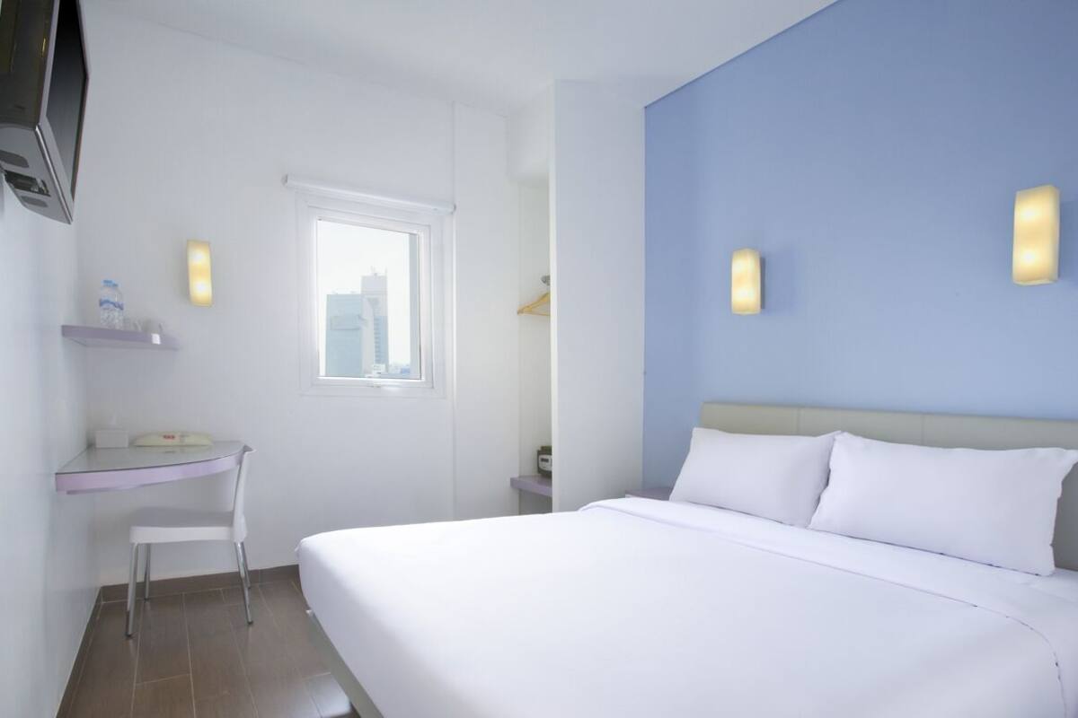 Ein Hotelzimmer mit einem Bett, einem Schreibtisch, einem Stuhl, einem Fernseher und einem Fenster mit Stadtblick.