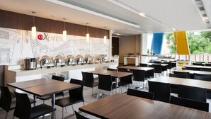 Een moderne cafeteria met meerdere tafels en stoelen, een buffetgedeelte met etenswaren en een groot raam met uitzicht op het buiten.