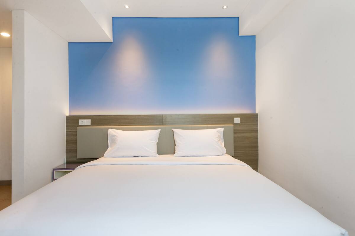 Ein modernes Hotelzimmer mit einem großen Bett, einem hölzernen Kopfteil und einer blauen Akzentwand.