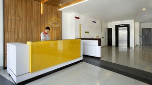 Een modern receptiegebied met een houten accentmuur, een geel receptiebalie en een strakke, betegelde vloer.