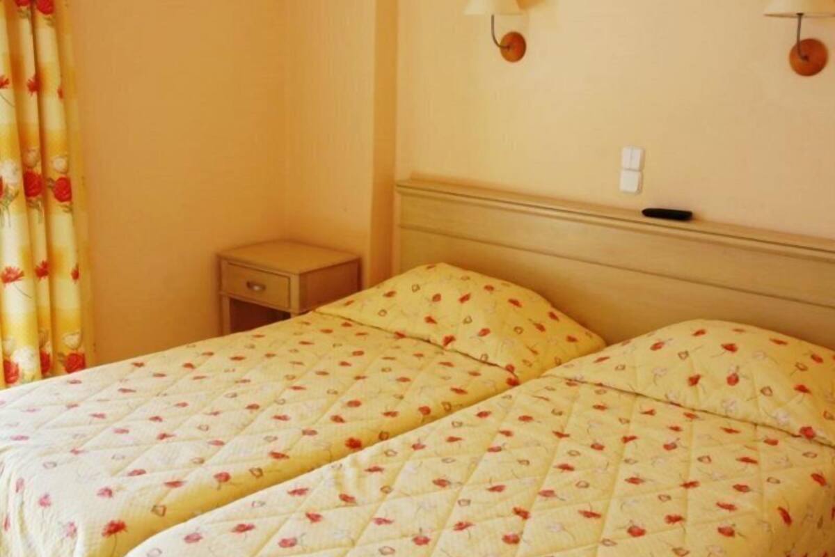 A room with two beds, each with a floral-patterned bedspread, a small bedside table, and a wall-mounted lamp.