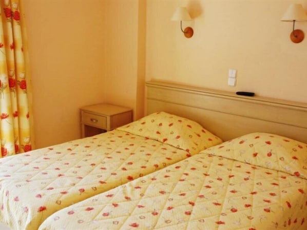 Una habitación con dos camas, cada una con una colcha de motivos florales, una mesita de noche pequeña y una lámpara de pared.
