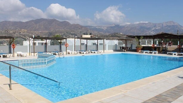 Una piscina con sillas de descanso y sombrillas, rodeada de montañas.