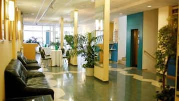 Un hall de hotel con mostrador de recepción, zona de estar y plantas en macetas.