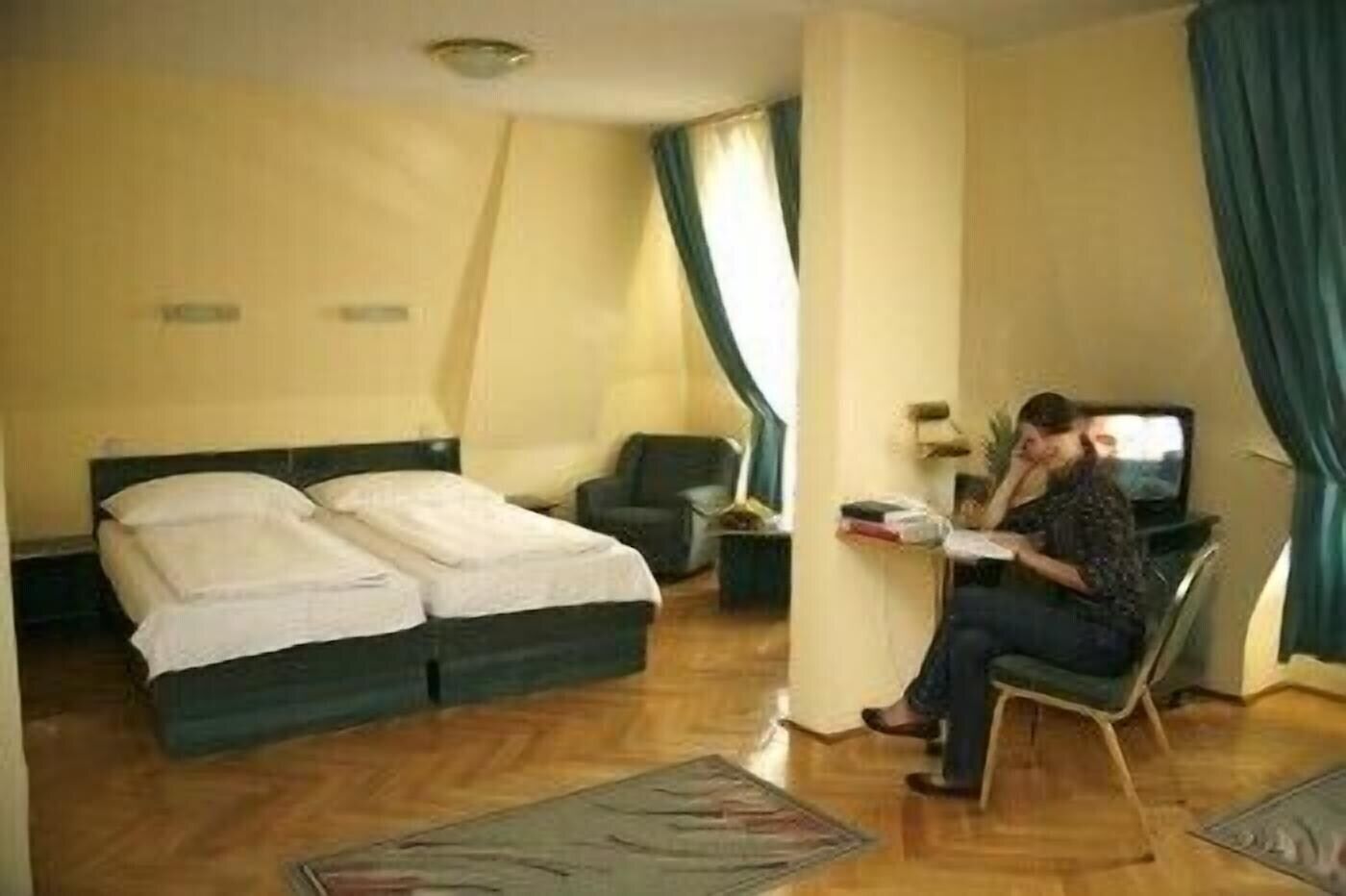 Una habitación de hotel con dos camas, un escritorio, una silla, un televisor y un ventanal con cortinas.