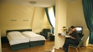 A hotel room with two beds, a desk, a chair, a TV, and a window with curtains. - Bara (Budapest)