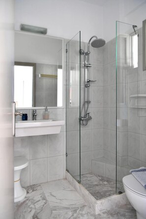 A modern bathroom with a glass-enclosed shower, a white sink, and a marble-tiled floor. - Sunsetview (Paros)