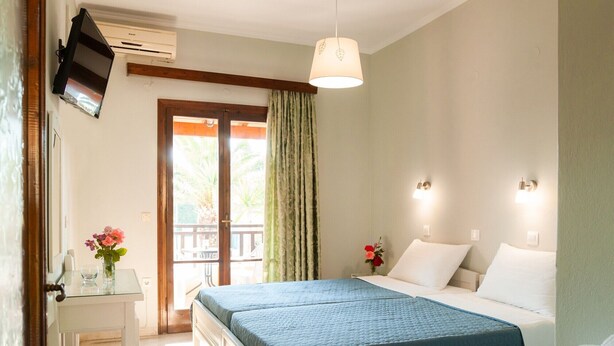 A bedroom with a bed, bedside tables, a desk, and a window with curtains. - Villa Eleni (Corfu)