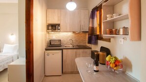 A compact kitchen with a microwave, toaster, sink, and a small refrigerator. There is a fruit bowl on the counter and a bottle of wine. - Villa Eleni (Corfu)
