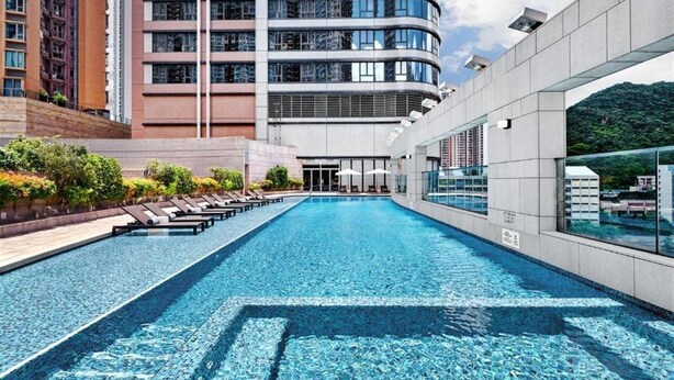 Un hôtel moderne doté d’une piscine, de chaises longues et offrant une vue sur les bâtiments environnants.
