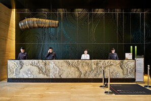 Un comptoir d’accueil avec quatre employés, un mur décoratif orné d’un élément suspendu, et un tapis noir avec du texte au sol.