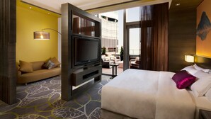 Une chambre d’hôtel avec un lit, une télévision, un canapé et un balcon donnant sur un immeuble.