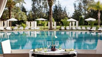 A poolside table with a green tablecloth, a bottle, and glasses, surrounded by lounge chairs and umbrellas.