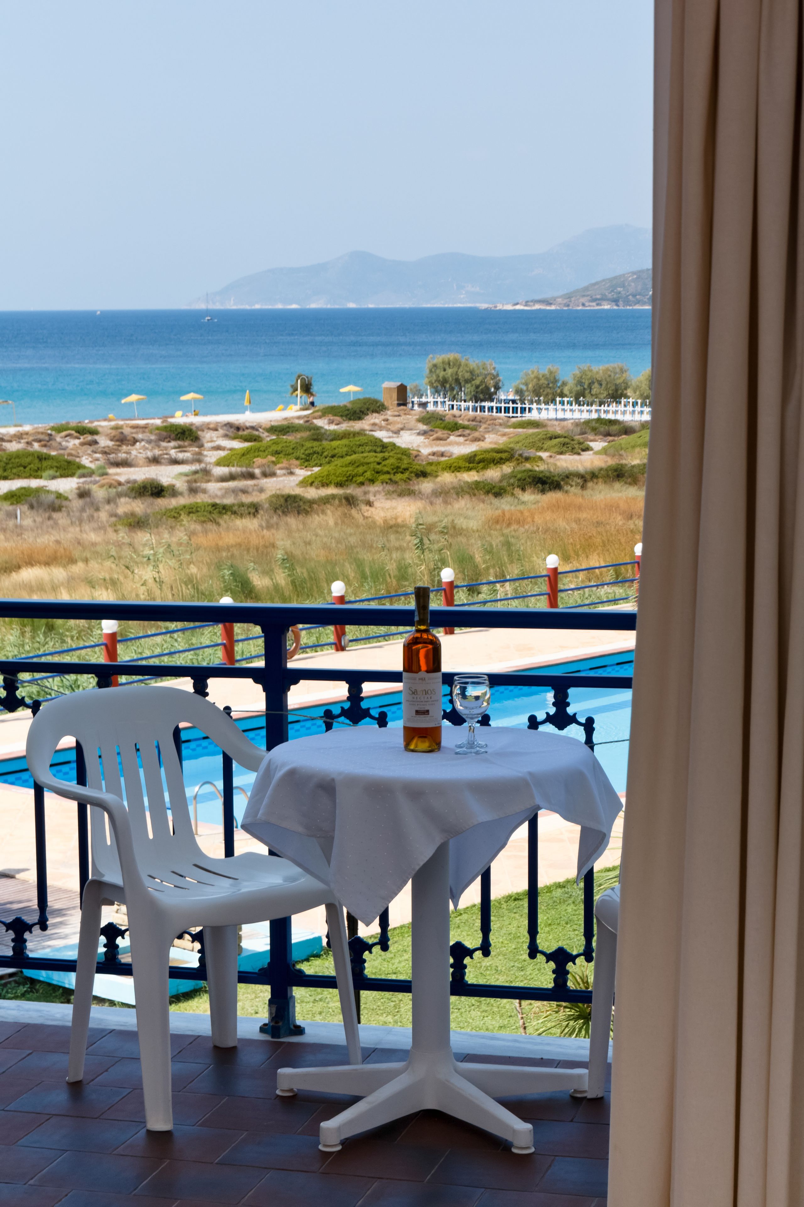 A balcony with a table and chairs overlooking a beach and ocean.