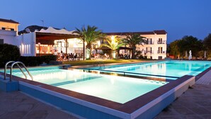 Une piscine dotée d’une terrasse carrelée, entourée de palmiers et bordée d’un immeuble avec de nombreux balcons.