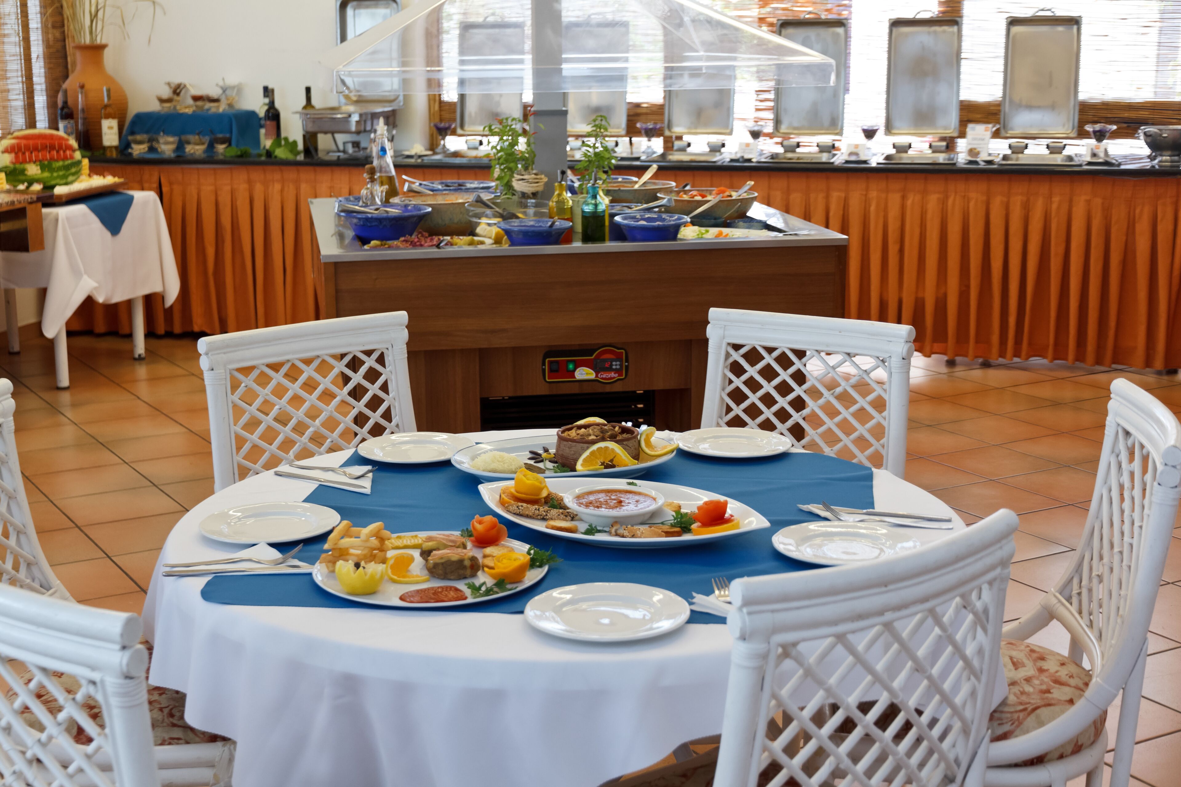A buffet setup with various dishes, a coffee machine, and a view of the kitchen in the background.