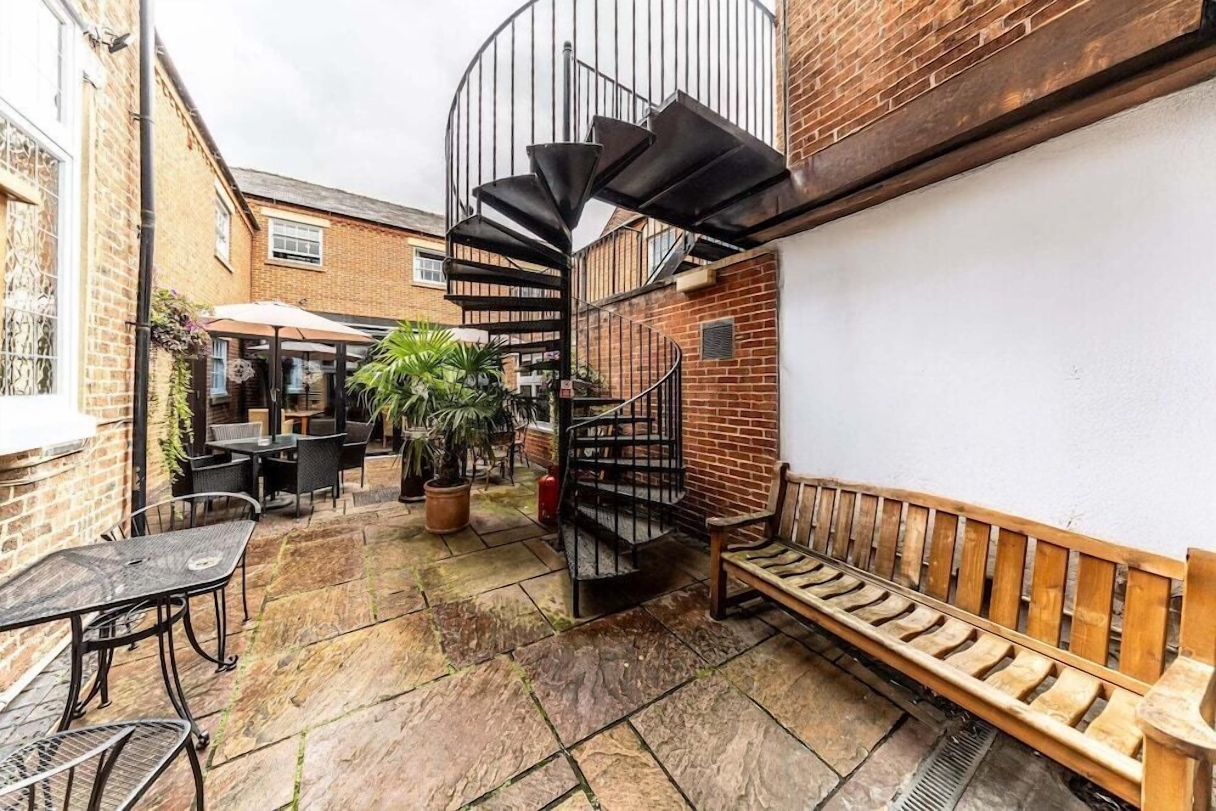 A courtyard with a spiral staircase, outdoor seating, and potted plants.