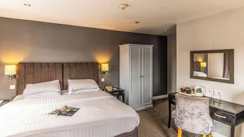 A hotel room with a large bed, bedside lamps, a wardrobe, a desk with a chair, and a mirror on the wall.