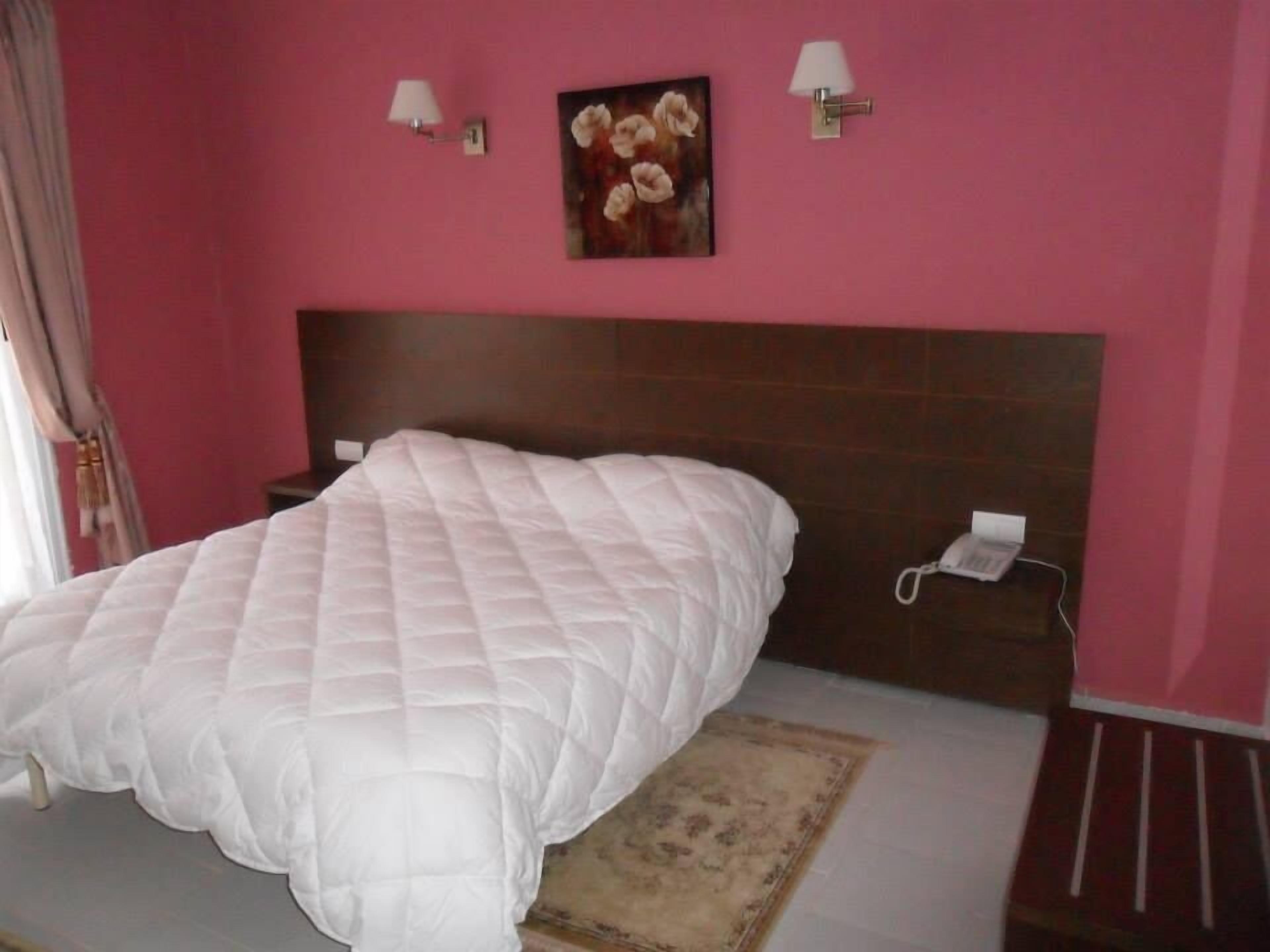 Un dormitorio con una cama grande, una mesita de noche, un teléfono y un cuadro en la pared.