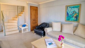 A living room with a staircase, a black leather armchair, a beige sofa, and a painting on the wall. - Efrosini Village (Kefalonia)