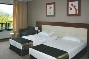 Une chambre d’hôtel avec deux lits, un bureau, une chaise, une fenêtre avec des rideaux et deux tableaux encadrés au mur.