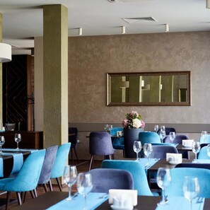 Ein Restaurant mit blauen Stühlen, Tischen und einem großen Spiegel an der Wand.