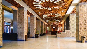 A spacious lobby with a high ceiling featuring intricate geometric patterns, a reception desk, and a seating area. - Hotel Les Zianides (Tlemcen)