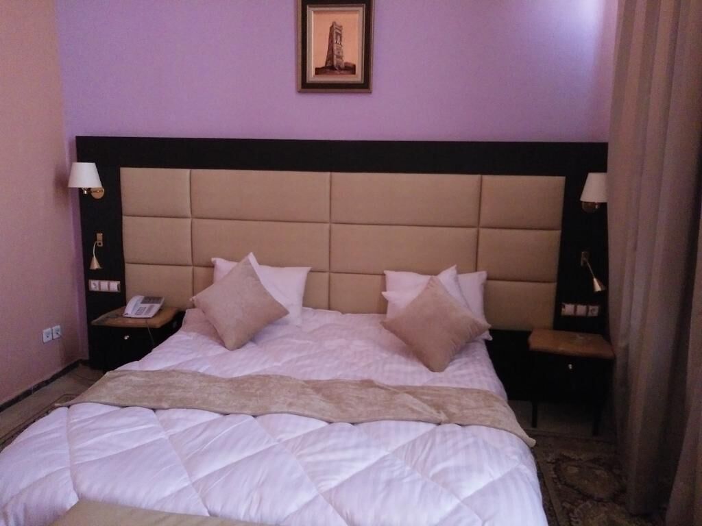 Une chambre d’hôtel avec un grand lit, deux tables de chevet, une tête de lit et un tableau encadré au mur.