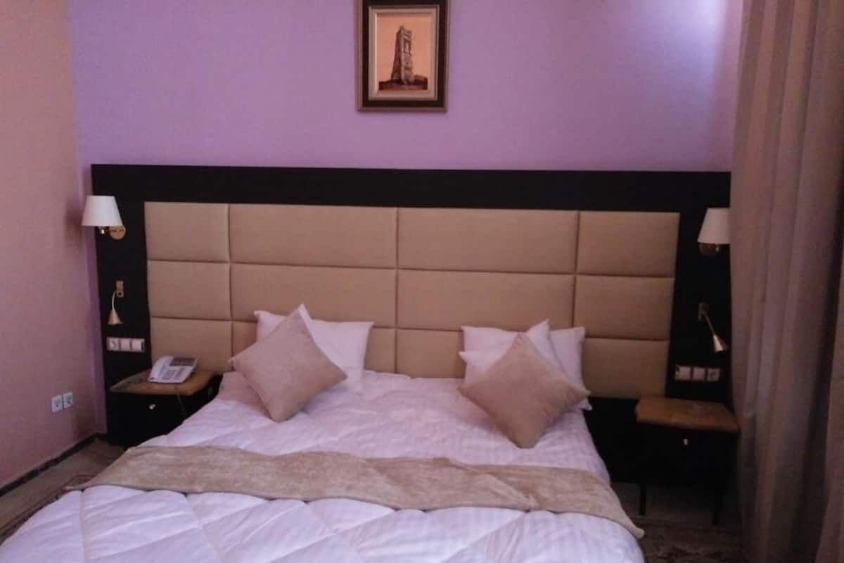 Une chambre d’hôtel avec un grand lit, deux tables de chevet, une tête de lit et un tableau encadré au mur.