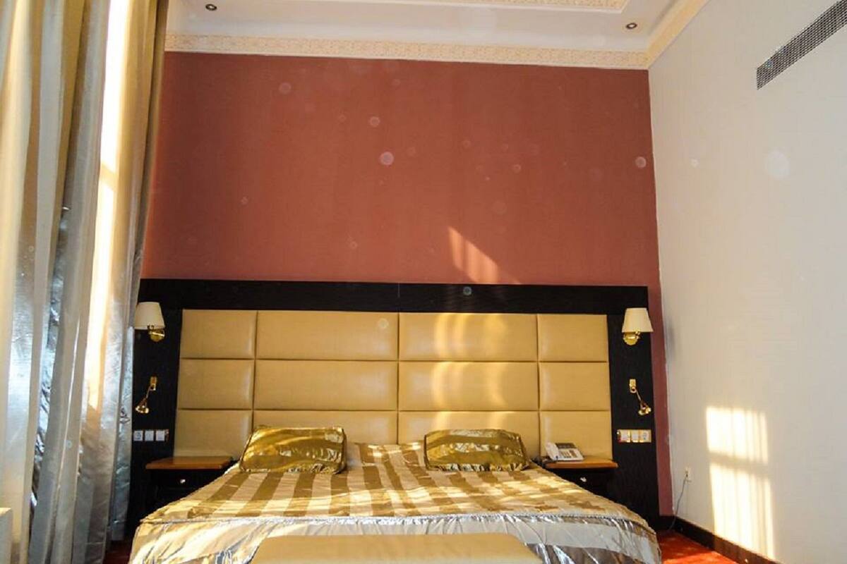 Une chambre d’hôtel avec un grand lit, une tête de lit, des lampes de chevet et une fenêtre avec des rideaux.