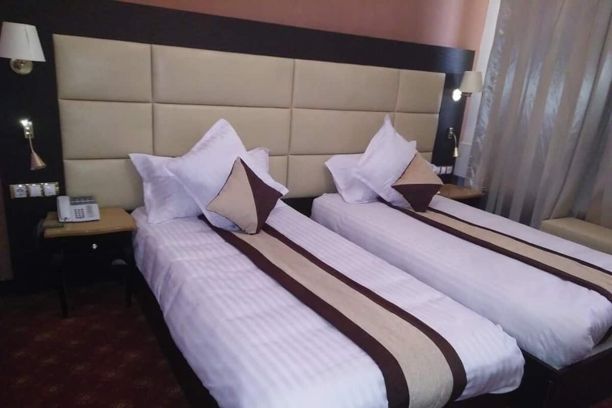 Une chambre d’hôtel avec deux lits, une tête de lit, des tables de chevet, des lampes et un téléphone.