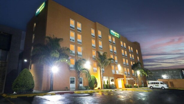 Un hotel de varios pisos con fachada plana, múltiples ventanas y un estacionamiento.
