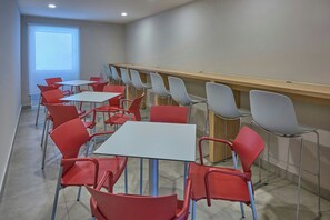 A modern dining area with red and grey chairs and white tables, arranged in rows.