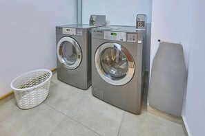 Deux machines à laver LG à chargement frontal, destinées à un usage commercial, se trouvent dans une buanderie équipée d’un panier à linge blanc.